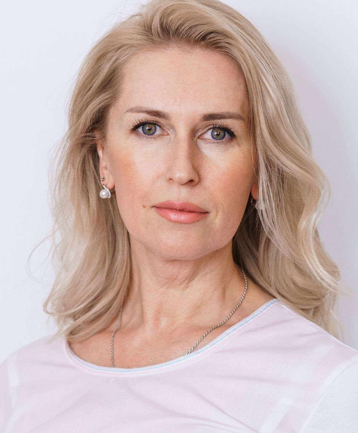 Smiling woman with blonde hair and pearl earrings.