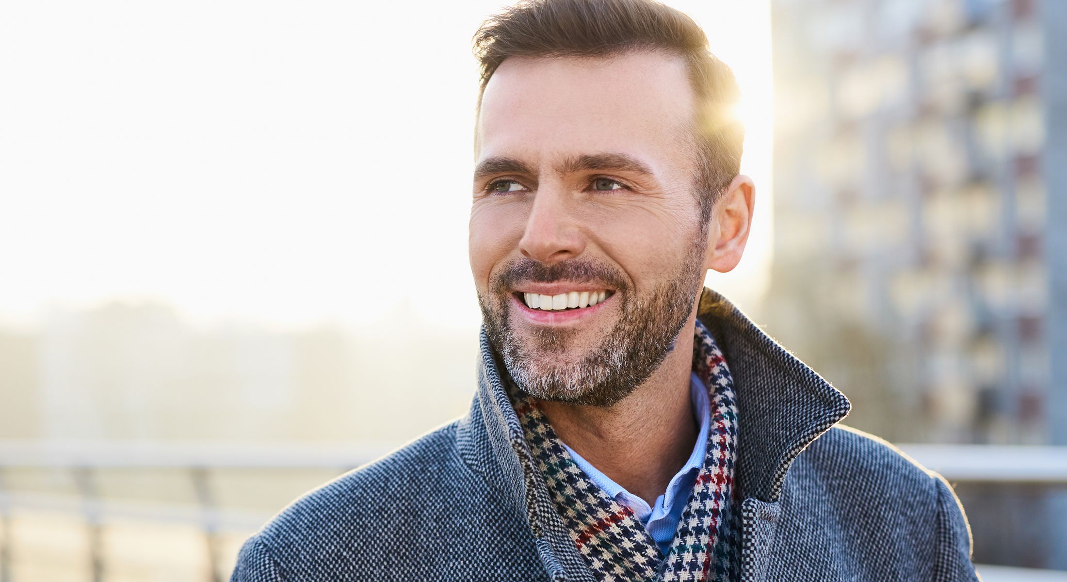 Smiling man wearing a stylish coat outdoors.