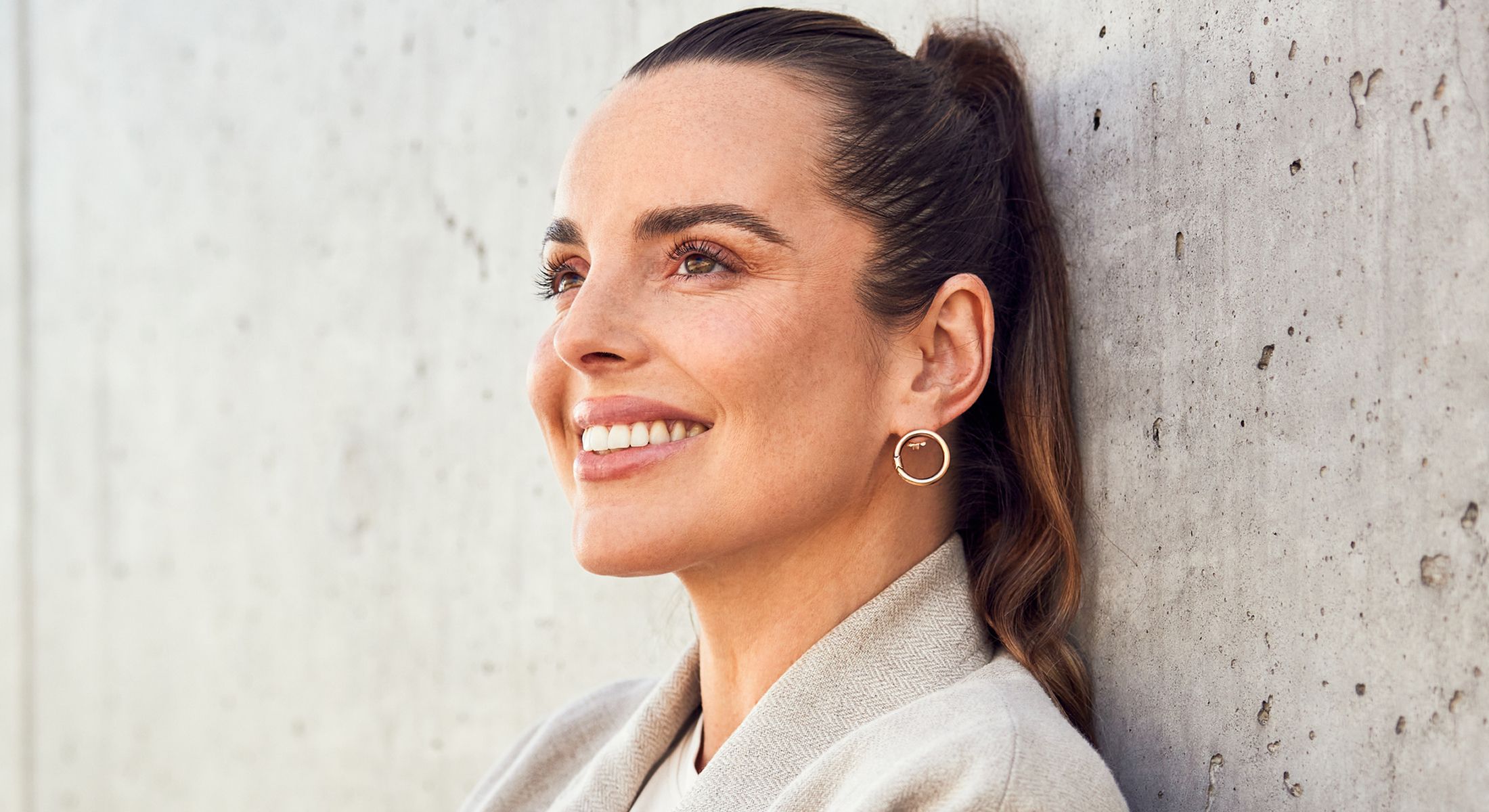 Smiling woman leaning against concrete wall.